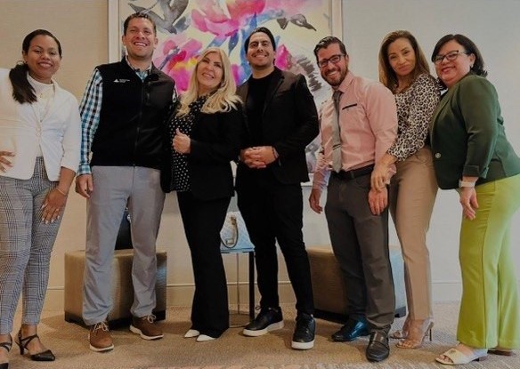 Equipo Legacy posando frente a un mural floral en evento corporativo
